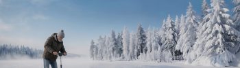 Designia ja graafista suunnittelua kuvaava mies kairaamassa jäätä talvisessa järvimaisemassa